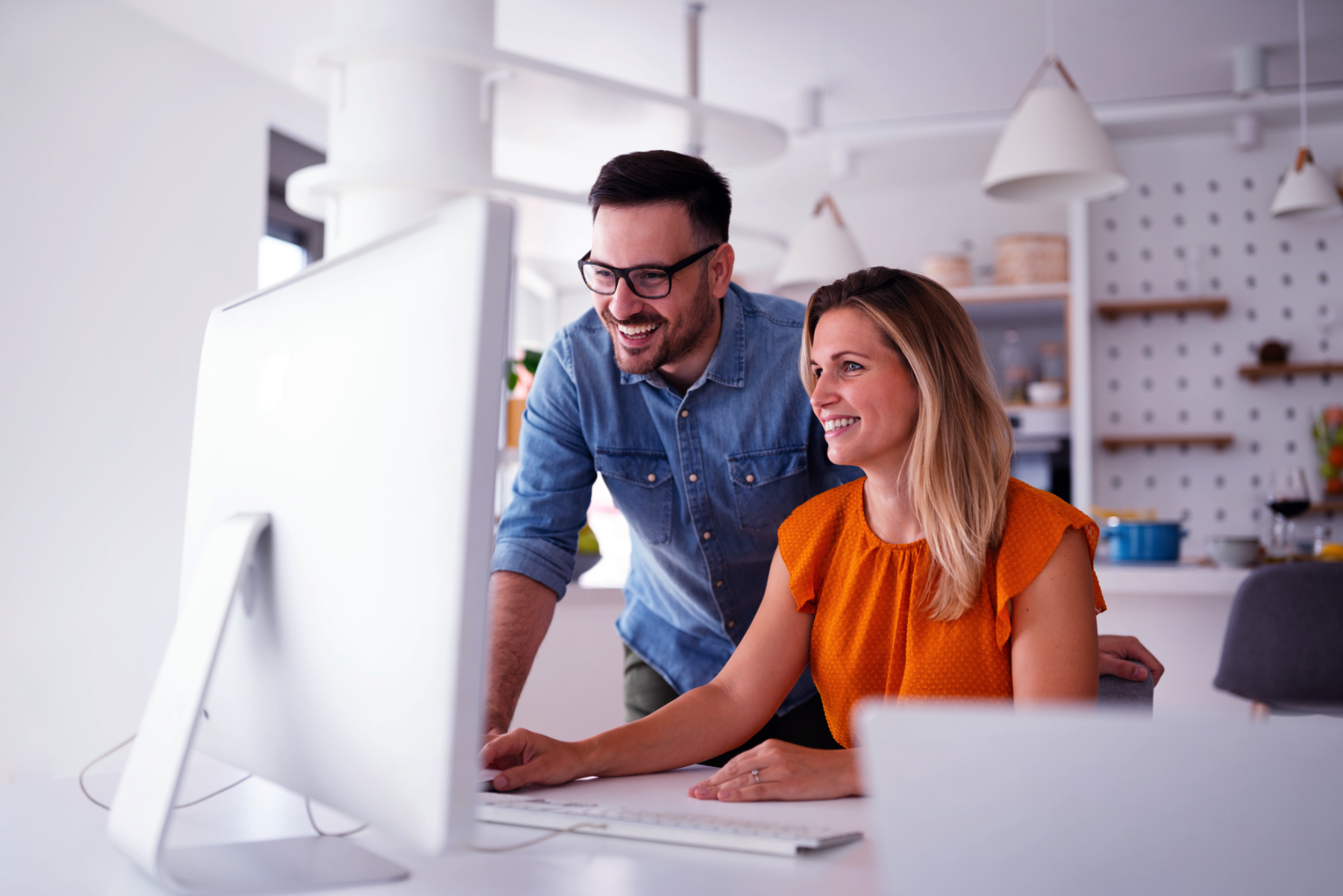 Two people are looking at a computer monitor and smiling in a modern, brightly lit office space, celebrating a new partnership for Custom Web design.